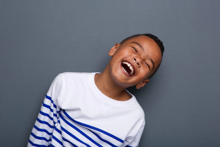A young boy with healthy teeth wearing a striped shirt, laughing joyfully.